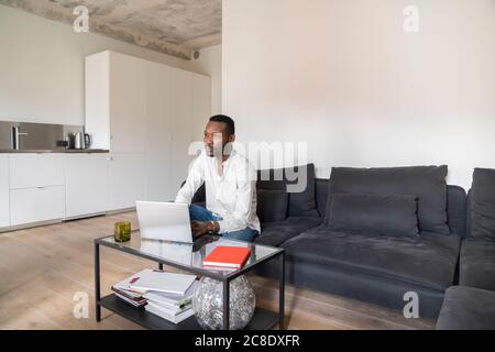 Pensive man sitting on couch in modern apartment using laptop Stock Photo