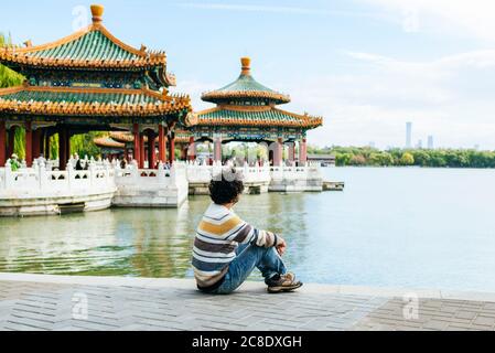 Man sitting on footpath by lake in Beihai Park, Beijing, China Stock Photo