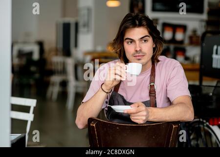 Thoughtful male owner drinking coffee while sitting on chair in cafe Stock Photo