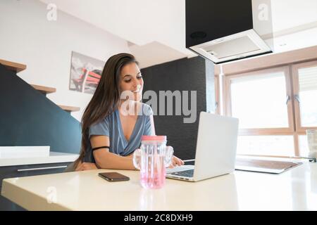 Smiling woman working over laptop on kitchen island at home Stock Photo