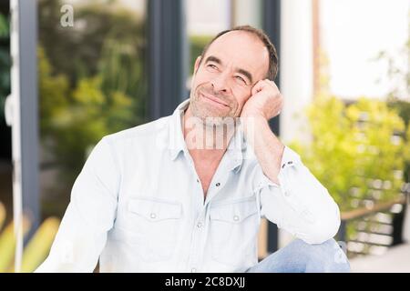 Thoughtful mature man looking away while sitting at back yard Stock Photo