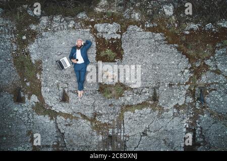 Aerial view of businessman wearing suit listening music while lying on land in forest Stock Photo