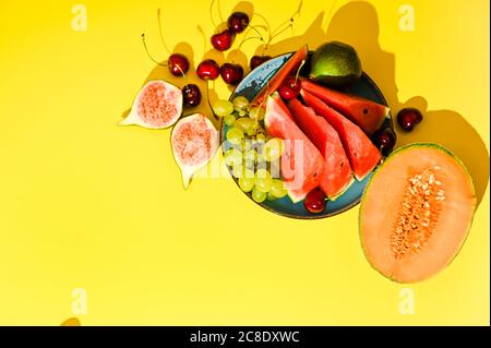Different fruits on a yellow background. Watermelon, melon, figs, grapes, cherries, juicy and ripe. Photo in hard light. High quality photo. Copy space. Above Stock Photo