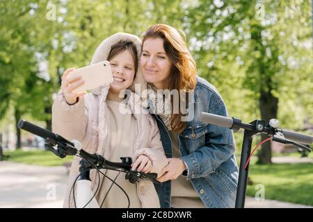 Girl taking selfie with mother while standing against trees in city park Stock Photo