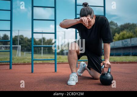 exhausted man athlete taking break between exercising with kettlebell outdoor Stock Photo