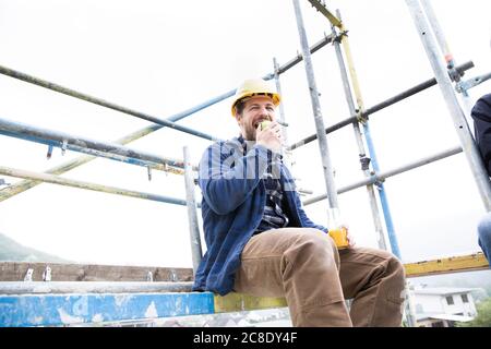 Construction worker eating food while sitting against clear sky at construction site Stock Photo
