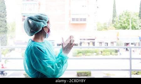 Female nurse wearing protective workwear clapping hands at window in hospital Stock Photo
