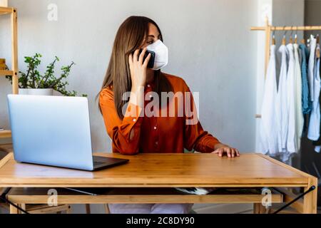 Female fashion designer on the phone at home wearing protective face mask