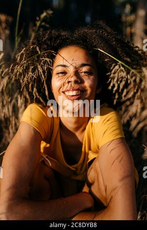 Close-up of smiling young woman with afro hair sitting in forest Stock Photo