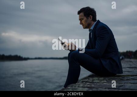 Mature businessman using tablet at the riverbank at dusk Stock Photo
