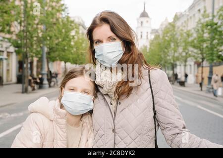 Mother and daughter wearing masks standing on street in city Stock Photo