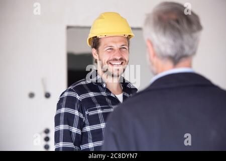Smiling construction worker wearing hardhat talking with architect in constructing home Stock Photo