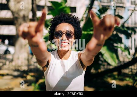 Close-up of smiling woman wearing sunglasses with arms raised standing outdoors Stock Photo
