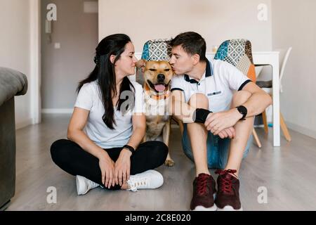 Couple kissing dog while sitting on floor at home Stock Photo