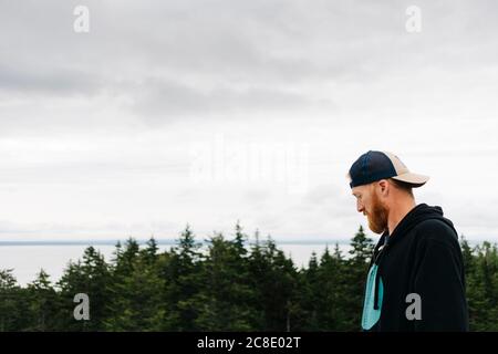 Bearded handsome man wearing cap at Bay of Fundy against sky Stock Photo