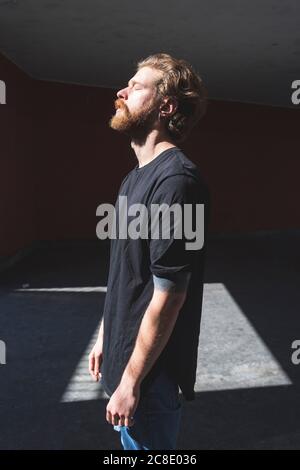 Bearded man with eyes closed standing against built structure on sunny day Stock Photo