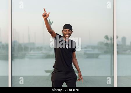 Smiling young man standing with arm raised against window Stock Photo