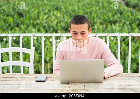 Teenage boy with short hair using laptop at table Stock Photo