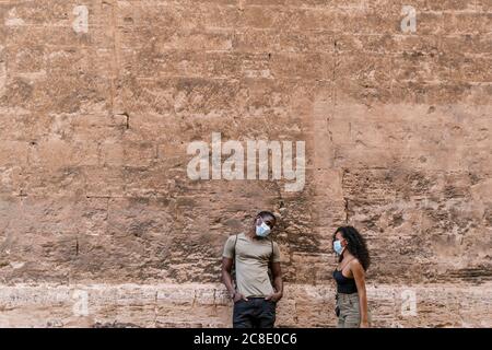 Man and woman wearing masks while talking against weathered wall Stock Photo