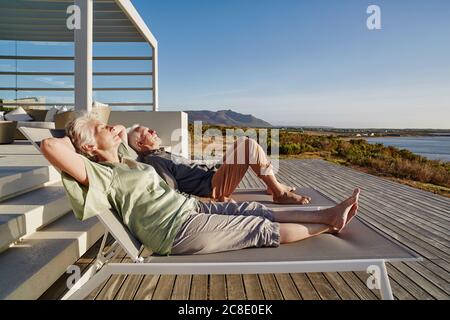 Senior couple lying on deck chairs at luxury beach house Stock Photo