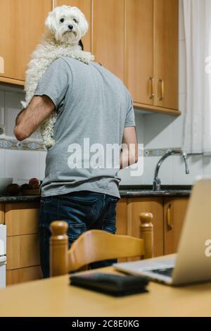 Man carrying dog while cooking in kitchen Stock Photo