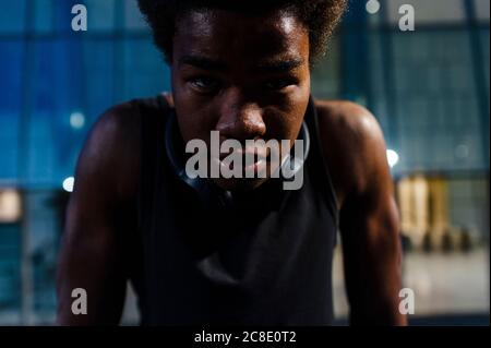 Portrait of a young athletic man with headphones at dusk in city