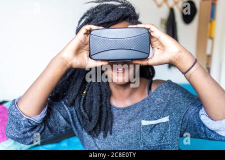 Young woman using virtual reality glasses sitting on bed Stock Photo