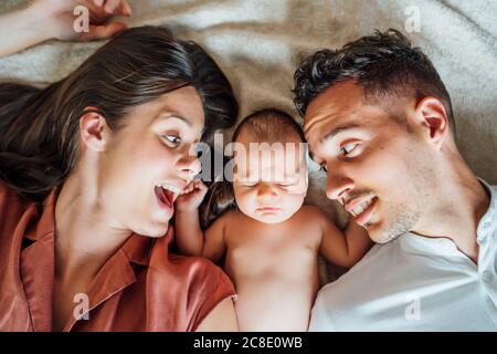 Cheerful parents lying with baby boy on bed at home