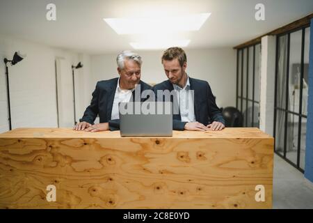 Two businesmen working at counter, looking at laptop, smiling Stock Photo