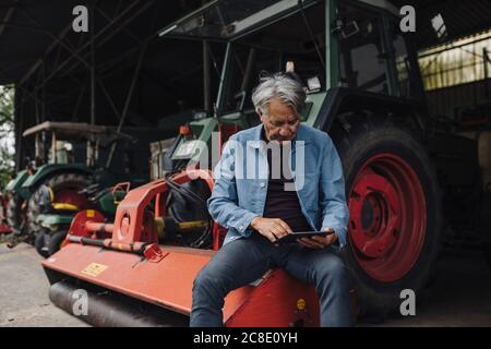 Senior man using tablet on a farm with tractor in barn Stock Photo