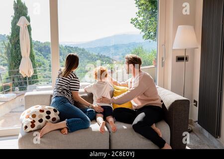 Family looking out through window while sitting on sofa in living room at home Stock Photo