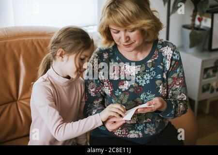 Girl and her grandmother making protective face mask at home during COVID-19 Stock Photo