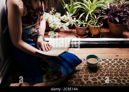Woman reading book while sitting on floor at home Stock Photo