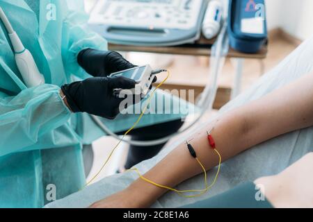 Doctor wearing protective clothes examining woman's arm with electrodes Stock Photo