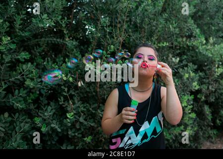 Teenager girl with down syndrome wearing 80's colorful make-up and clothes blowing soap bubble Stock Photo