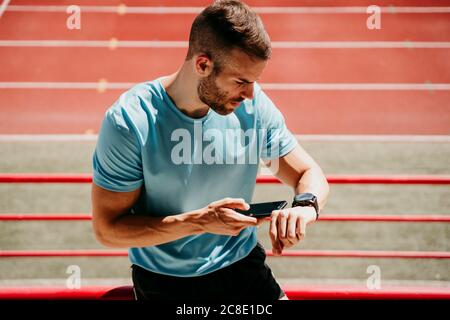 Male athlete in stadium checking smartwatch and smartphone Stock Photo