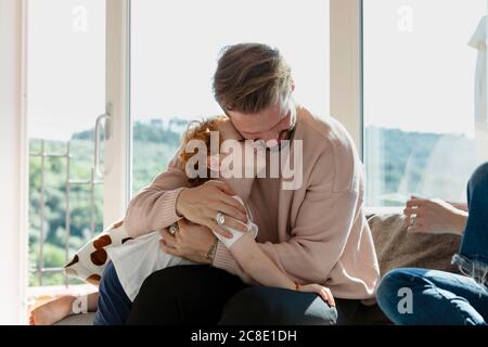 Man embracing cute preschool son while sitting by woman in living room at home Stock Photo