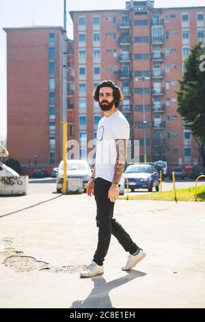 Bearded young man walking on road in city during sunny day Stock Photo
