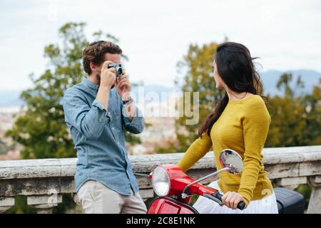 Young man photographing girlfriend sitting on Vespa Stock Photo