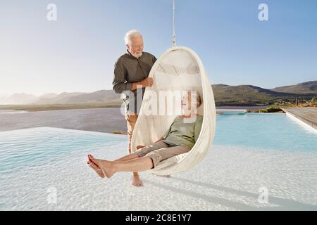 Happy senior couple with woman sitting in hanging chair above swimming pool Stock Photo