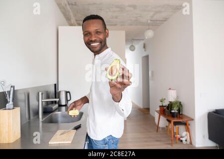 Portrait of smiling man with sliced avocado in his kitchen Stock Photo