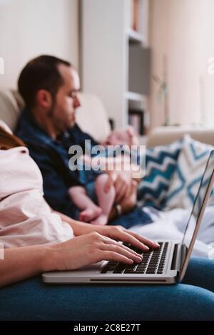 Mother using laptop while father carrying daughter in background Stock Photo
