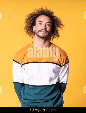 Handsome young man with curly hair standing against yellow background Stock Photo
