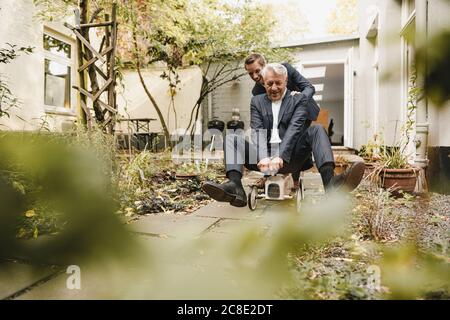 Businessman pushing senior partner on toy car through backyard Stock Photo