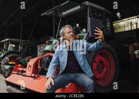 Senior man using tablet on a farm with tractor in barn Stock Photo