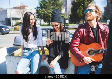 Bearded man playing guitar while standing with female friends in city Stock Photo