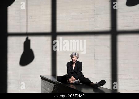 Female professional wearing black suit relaxing against sunlight and shadow in background at office Stock Photo