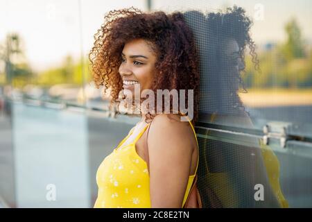 Close-up of smiling young woman with afro hair looking away while standing by wall