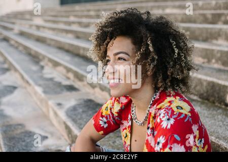 Thoughtful young woman smiling while sitting on steps during sunny day