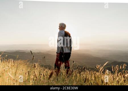 Active senior male hiker standing on mountain while looking at landscape during sunset Stock Photo